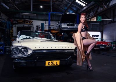 image of a woman with red hair wearing black lingerie standing next to a white Thunderbird Vintage Car